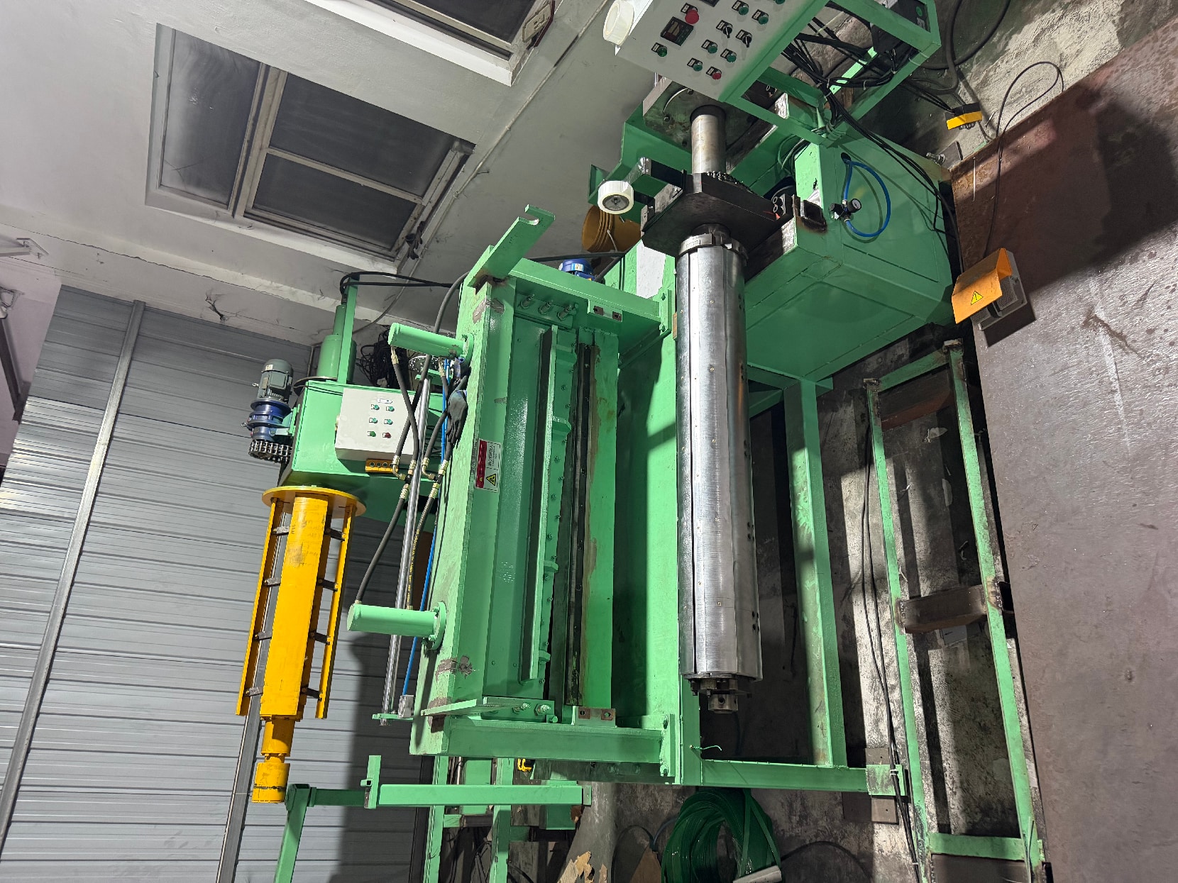 Green machine with a vertical mandrel and a yellow hydraulic column in the workshop